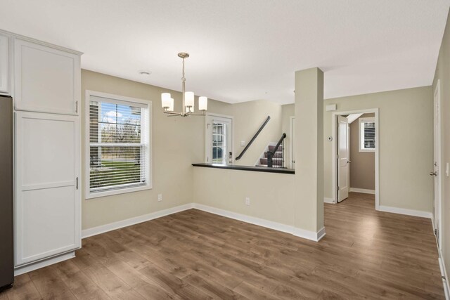 unfurnished dining area with dark wood-style flooring, baseboards, and a chandelier