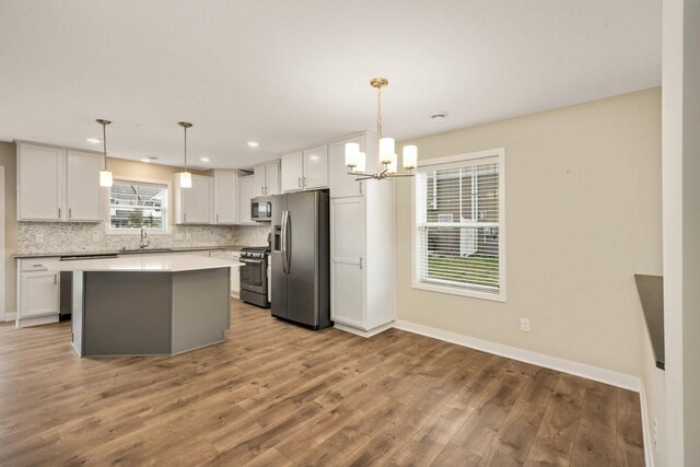 kitchen featuring backsplash, wood finished floors, a sink, a notable chandelier, and stainless steel appliances