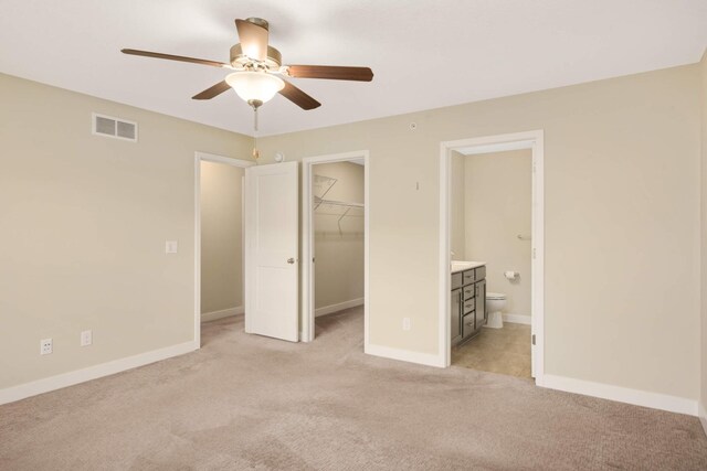 unfurnished bedroom featuring light colored carpet, visible vents, a closet, a spacious closet, and ensuite bathroom