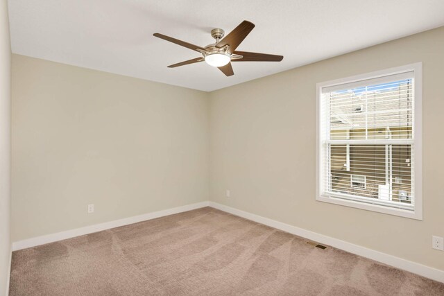 spare room featuring light colored carpet, baseboards, ceiling fan, and visible vents