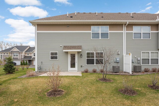 rear view of house with a yard, roof with shingles, central AC, and a patio area