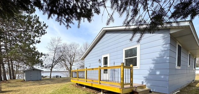rear view of house featuring a deck, an outdoor structure, a yard, and a shed