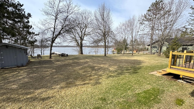 view of yard featuring a storage shed, a deck with water view, and an outbuilding