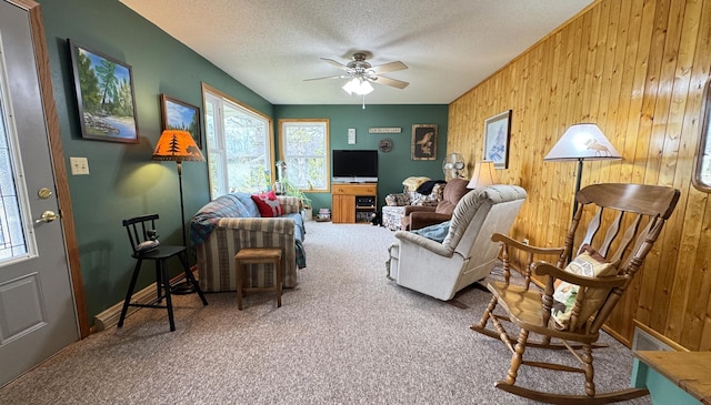living room with wood walls, carpet floors, ceiling fan, and a healthy amount of sunlight