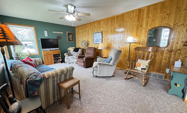 carpeted living area with wood walls, a ceiling fan, a textured ceiling, and visible vents