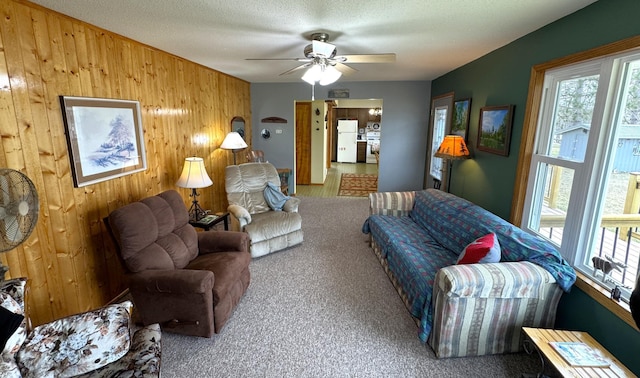 carpeted living area with wood walls and ceiling fan