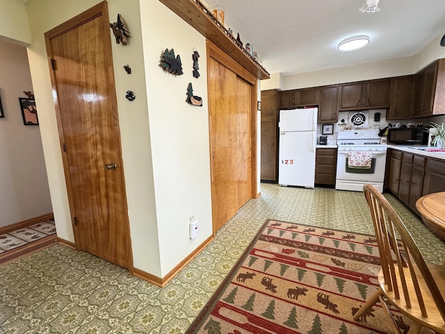 kitchen featuring light floors, light countertops, dark brown cabinets, white appliances, and baseboards