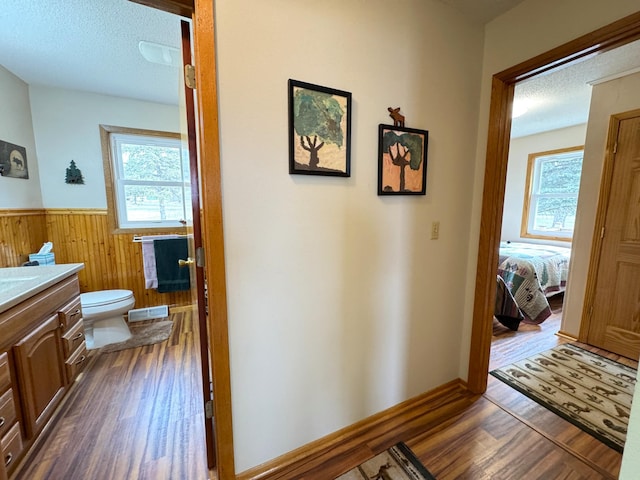 hall with dark wood-style floors, a textured ceiling, wainscoting, wood walls, and visible vents