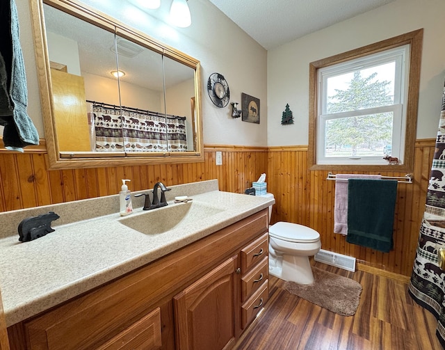full bathroom with wooden walls, wood finished floors, visible vents, toilet, and wainscoting