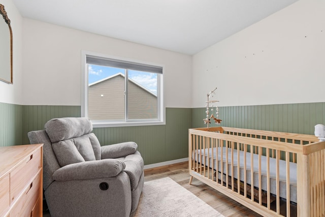 907 7th Ave, Wanamingo, MN 55983 - bedroom with wainscoting, wood finished floors, a crib, and baseboards