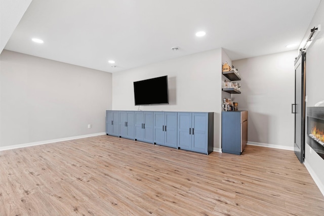 907 7th Ave, Wanamingo, MN 55983 - unfurnished living room with light wood-style flooring, recessed lighting, a barn door, and baseboards