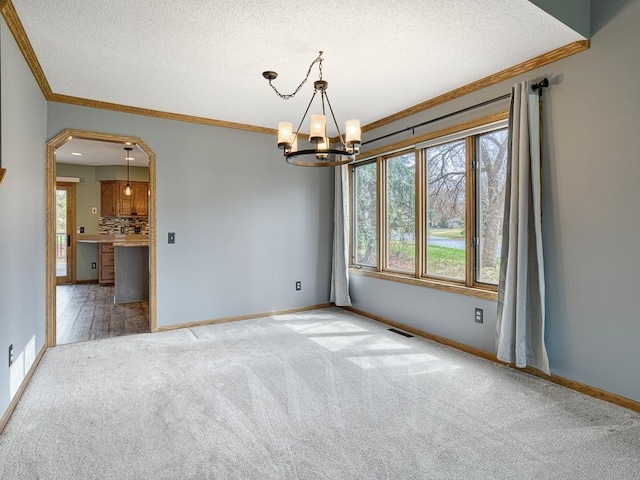 spare room featuring arched walkways, carpet floors, crown molding, and a notable chandelier