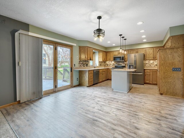 kitchen with light wood finished floors, stainless steel appliances, decorative backsplash, brown cabinetry, and light countertops
