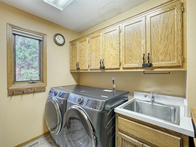 laundry area featuring cabinet space, washer and clothes dryer, a textured ceiling, and a sink