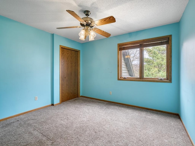 carpeted spare room featuring baseboards, a ceiling fan, and a textured ceiling