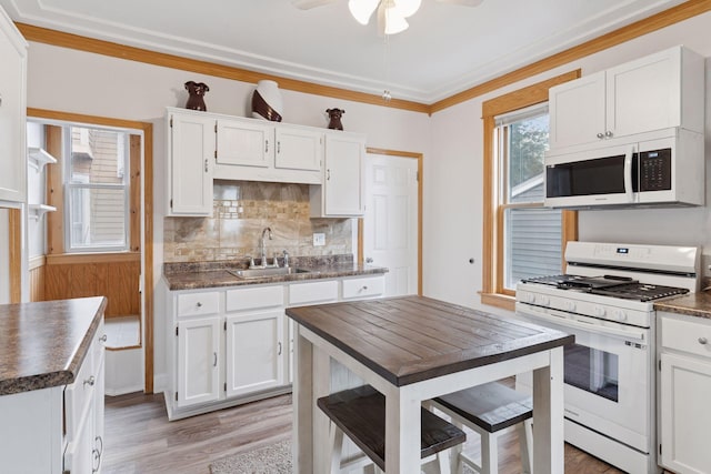 kitchen with white appliances, dark countertops, a sink, and light wood-style floors