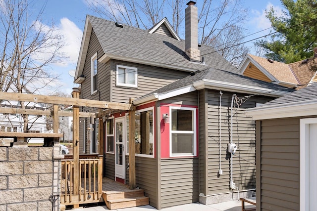 rear view of property featuring a chimney, a shingled roof, and a deck