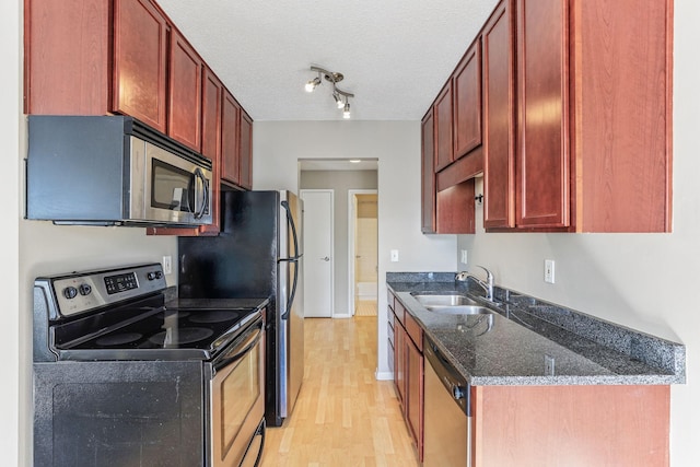 kitchen featuring stainless steel appliances, a sink, dark stone counters, dark brown cabinets, and light wood-style floors