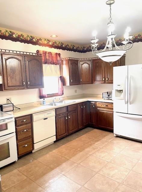 kitchen featuring an inviting chandelier, light countertops, a sink, and white appliances