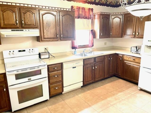 kitchen with white appliances, a sink, range hood, and light countertops