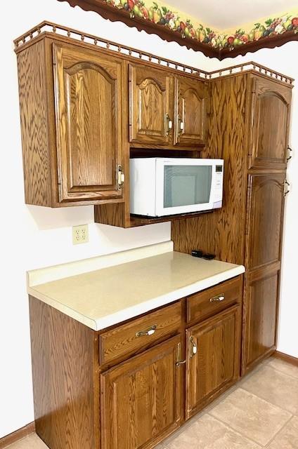 kitchen featuring brown cabinetry, light countertops, baseboards, and white microwave