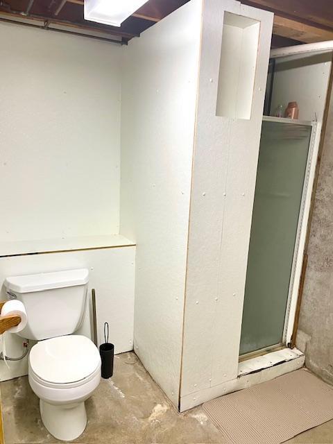 bathroom featuring concrete flooring, toilet, and a shower stall