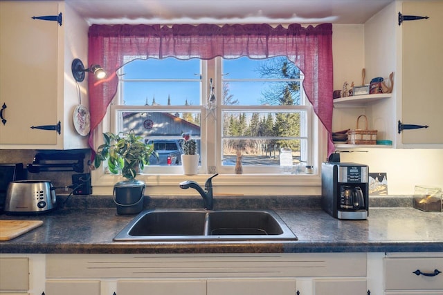 kitchen with white cabinets, dark countertops, open shelves, and a sink