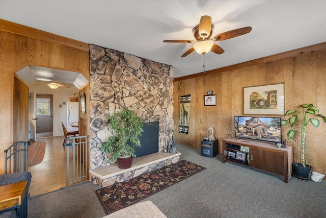 interior space with carpet, a stone fireplace, wood walls, and ceiling fan