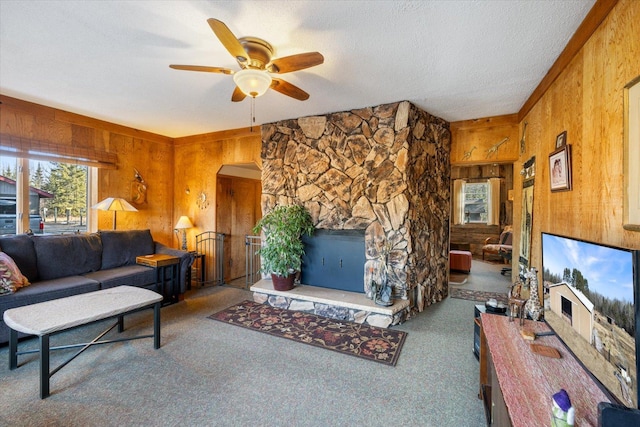 living area with arched walkways, a ceiling fan, wood walls, and carpet floors