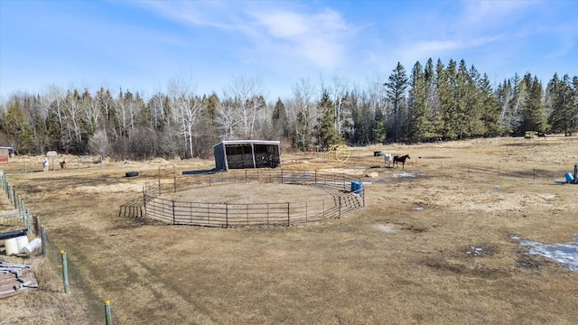 view of yard featuring an exterior structure, fence, a rural view, a view of trees, and an outdoor structure