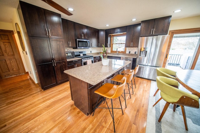 1474 Aldrich Ct, Faribault, MN 55021 - kitchen with appliances with stainless steel finishes, a center island, a breakfast bar, tasteful backsplash, and light wood-type flooring