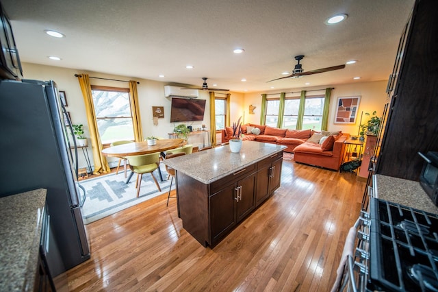 1474 Aldrich Ct, Faribault, MN 55021 - kitchen with freestanding refrigerator, a wall unit AC, a healthy amount of sunlight, ceiling fan, and a kitchen island