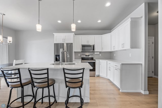kitchen with a sink, stainless steel appliances, light wood-style floors, a kitchen breakfast bar, and white cabinets