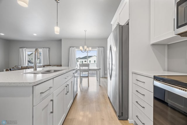 kitchen featuring light stone counters, appliances with stainless steel finishes, white cabinets, a sink, and a notable chandelier