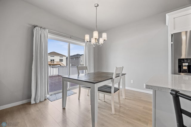 dining space featuring a chandelier, baseboards, and light wood finished floors