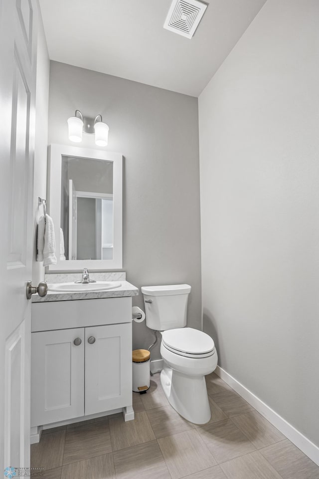 half bath featuring baseboards, visible vents, toilet, and vanity
