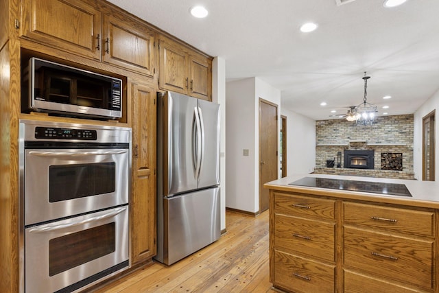 13982 Mount Ter, Minnetonka, MN 55345 - kitchen featuring appliances with stainless steel finishes, brown cabinets, light wood-style floors, open floor plan, and a fireplace