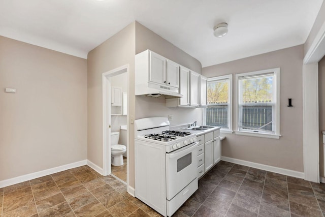 kitchen with gas range gas stove, under cabinet range hood, baseboards, and white cabinets