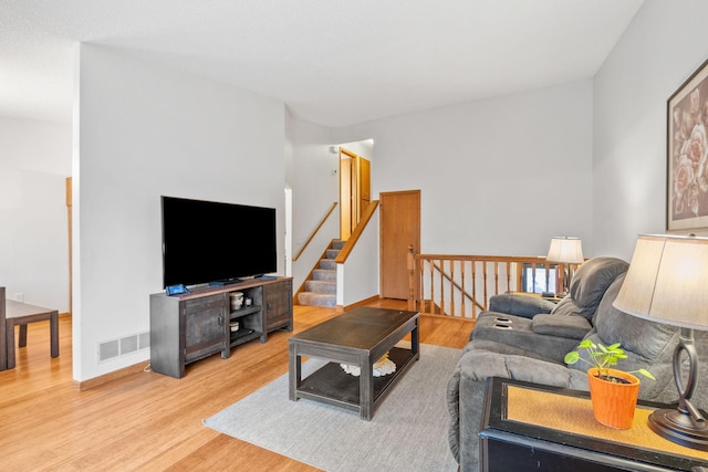 living room with wood finished floors, visible vents, baseboards, and stairs