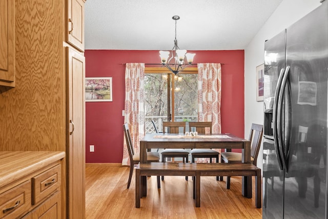 dining area with baseboards, an inviting chandelier, a textured ceiling, and light wood-type flooring