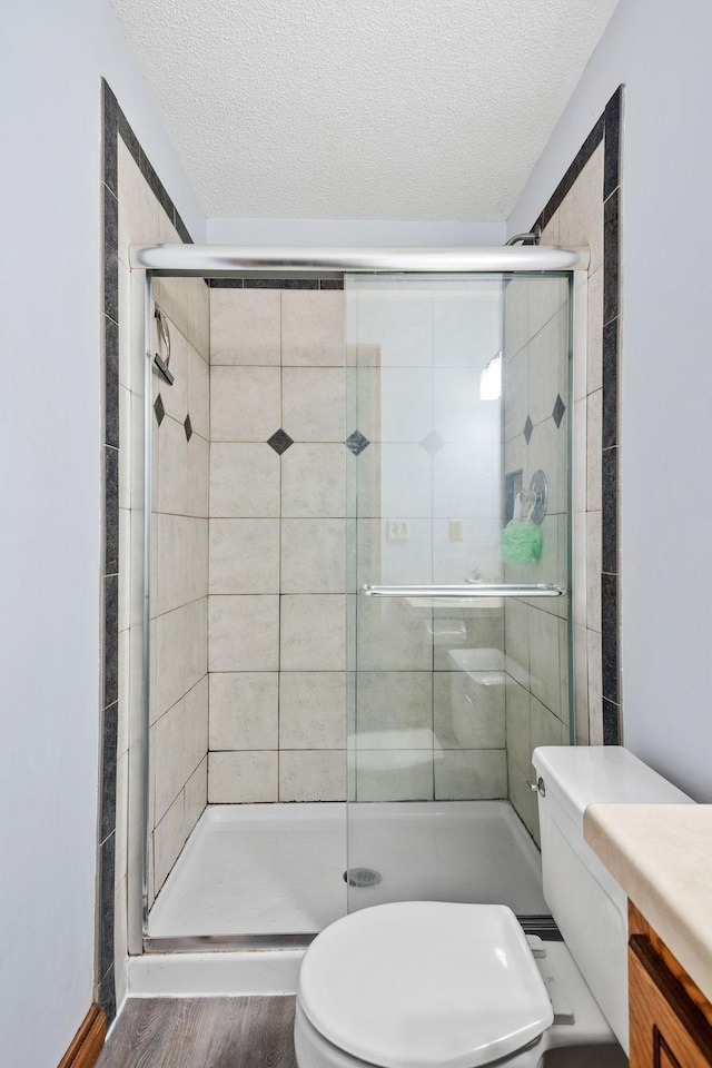 bathroom featuring a shower stall, a textured ceiling, toilet, and wood finished floors