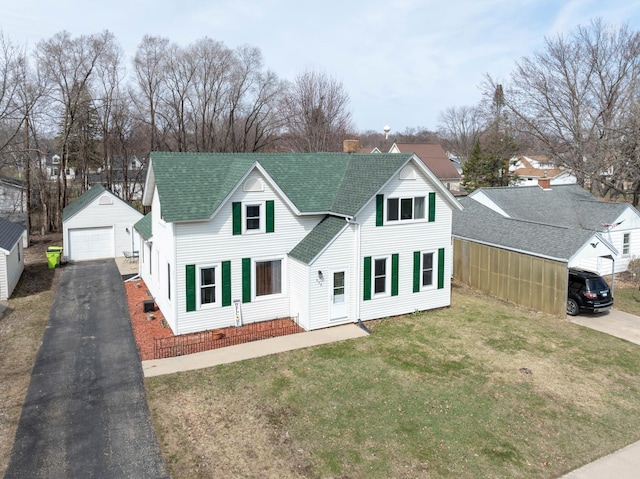 view of front of home featuring a front lawn, driveway, an outbuilding, a garage, and roof with shingles
