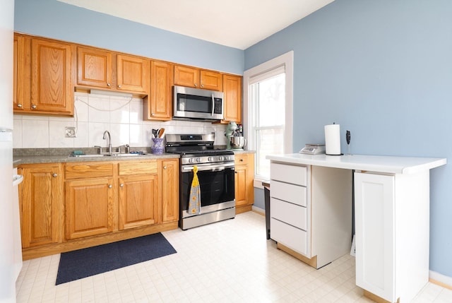 kitchen featuring stainless steel appliances, a sink, decorative backsplash, brown cabinets, and light floors