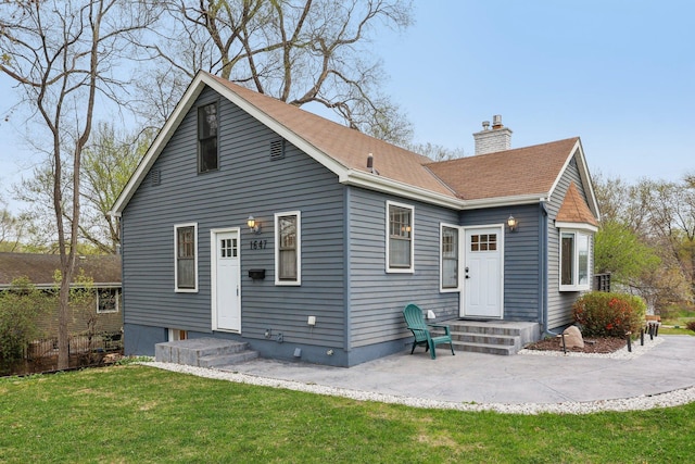 rear view of house with a yard, a chimney, a patio area, and roof with shingles