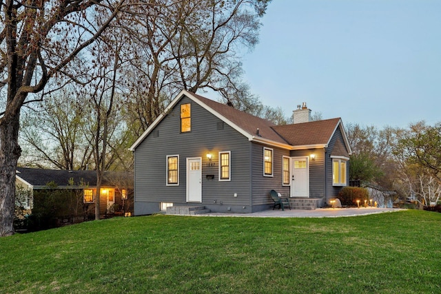 back of property with entry steps, a chimney, and a yard
