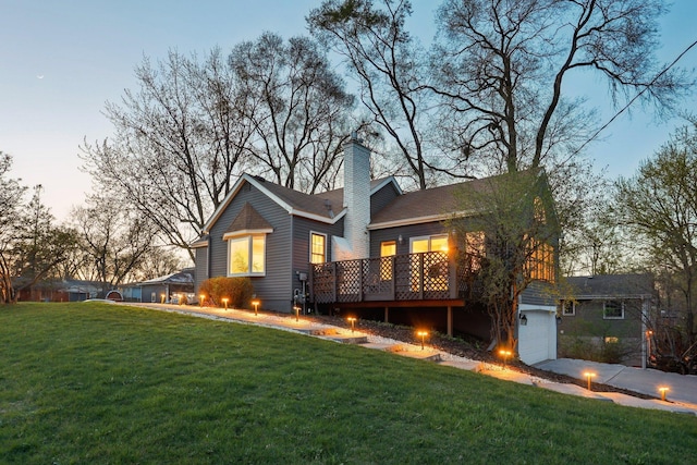 rear view of property featuring a garage, a chimney, a yard, and a deck
