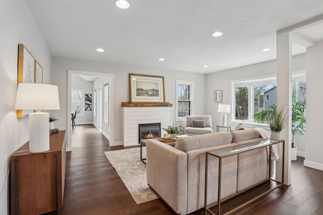 living area with a glass covered fireplace, recessed lighting, baseboards, and dark wood finished floors