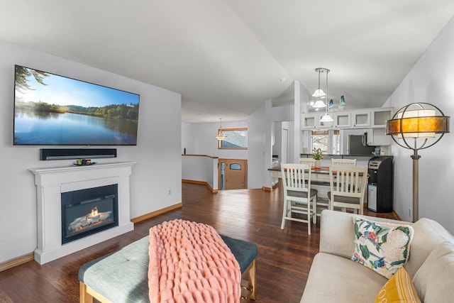living area featuring lofted ceiling, a glass covered fireplace, baseboards, and dark wood-type flooring