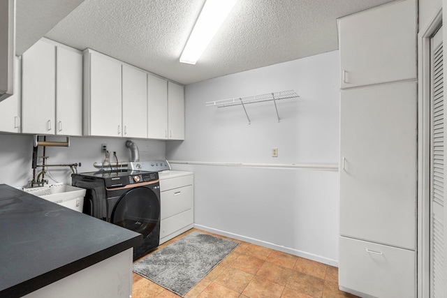 laundry area with a sink, a textured ceiling, separate washer and dryer, cabinet space, and baseboards