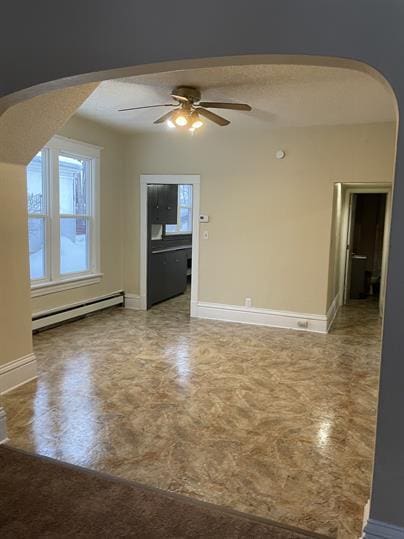 spare room featuring a baseboard heating unit, arched walkways, baseboards, and ceiling fan